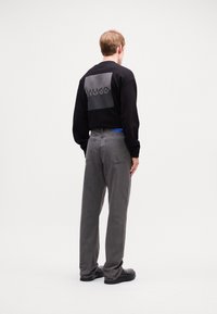 Black sweatshirt with a gray logo panel, paired with dark gray jeans and black shoes, showing a relaxed fit and minimalistic design.