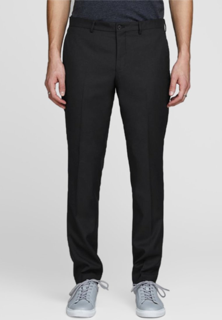 Pantalons noirs ajustés, dotés de poches latérales, d'un devant plat et d'une texture lisse, associés à des baskets gris clair.