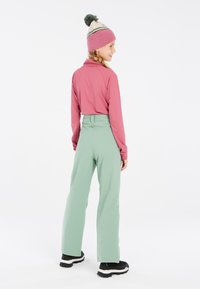 Un haut rose à manches longues associé à un pantalon vert menthe taille haute et des bottes noires, complété par un bonnet rose clair avec un pompon vert.