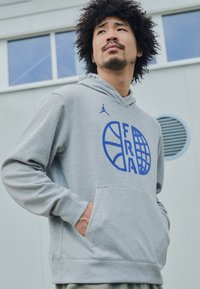 Felpa grigia con cappuccio, decorata con una grafica blu di un pallone da basket e le lettere "FRA" sul davanti. Tasche a marsupio incluse.