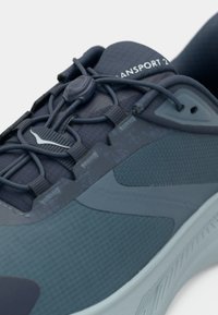 Σκούρο μπλε αθλητικό παπούτσι με υφασμάτινη υφή, κορδόνια γρήγορης σύσφιξης και την ένδειξη "Transport 2" στο γλώσσα.