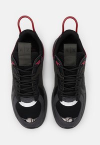 Chaussures de sport noires et grises avec tige en maille et synthétique, ornées d'accents rouges, de détails réfléchissants et de semelles texturées.