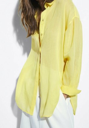 Transparante gele blouse met knopen, een losse pasvorm, lange mouwen, een enkele borstzak en een afgeronde zoom, gemaakt van lichtgewicht stof.