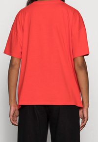Camiseta de algodón roja con mangas cortas y un corte relajado, que presenta un corte recto y un diseño minimalista, combinada con pantalones negros.