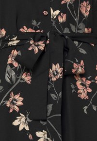 Tissu noir avec imprimé floral pêche et crème, présentant une ceinture nouée à la taille et un petit bouton rond au centre devant.