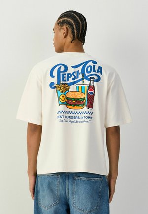 Person mit geflochtenem Haar, der ein weißes Hemd mit einem Pepsi-Cola-Grafikdruck trägt, der Pommes, Burger, Getränk und Pepsi-Flasche von hinten zeigt.