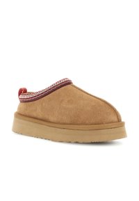 Brun ruskinds slip-on sko med en tykk gummisål og rød- og hvidbroderet kant omkring ankelkraven.