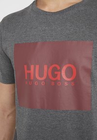 Dark gray cotton t-shirt featuring a large maroon rectangular graphic with the text "HUGO" in bold red and "HUGO BOSS" in smaller red font.