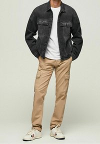 Svart denimjacka över en vit t-shirt, kombinerad med beige cargobyxor och vita sneakers. Har två bröstfickor och en avslappnad passform.