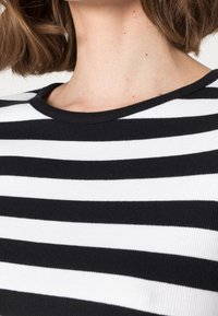 Svart- och vitrandig stickad topp med rund halsringning och ribbad struktur, med växlande breda och smala ränder.