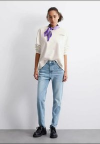 Ανοιχτόχρωμο κρέμ μπλουζάκι μακρύ μανίκι, σε χαλαρή γραμμή, συνδυασμένο με ανοιχτό μπλε τζιν ίσιων γραμμών. Ένα μωβ μαντήλι προσθέτει λεπτομέρεια. Μαύρα παπούτσια ολοκληρώνουν το σύνολο.