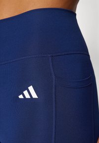 Marineblå leggings laget av elastisk stoff, med en hvit logo, en liten lomme og flate sømmer for komfort og holdbarhet.