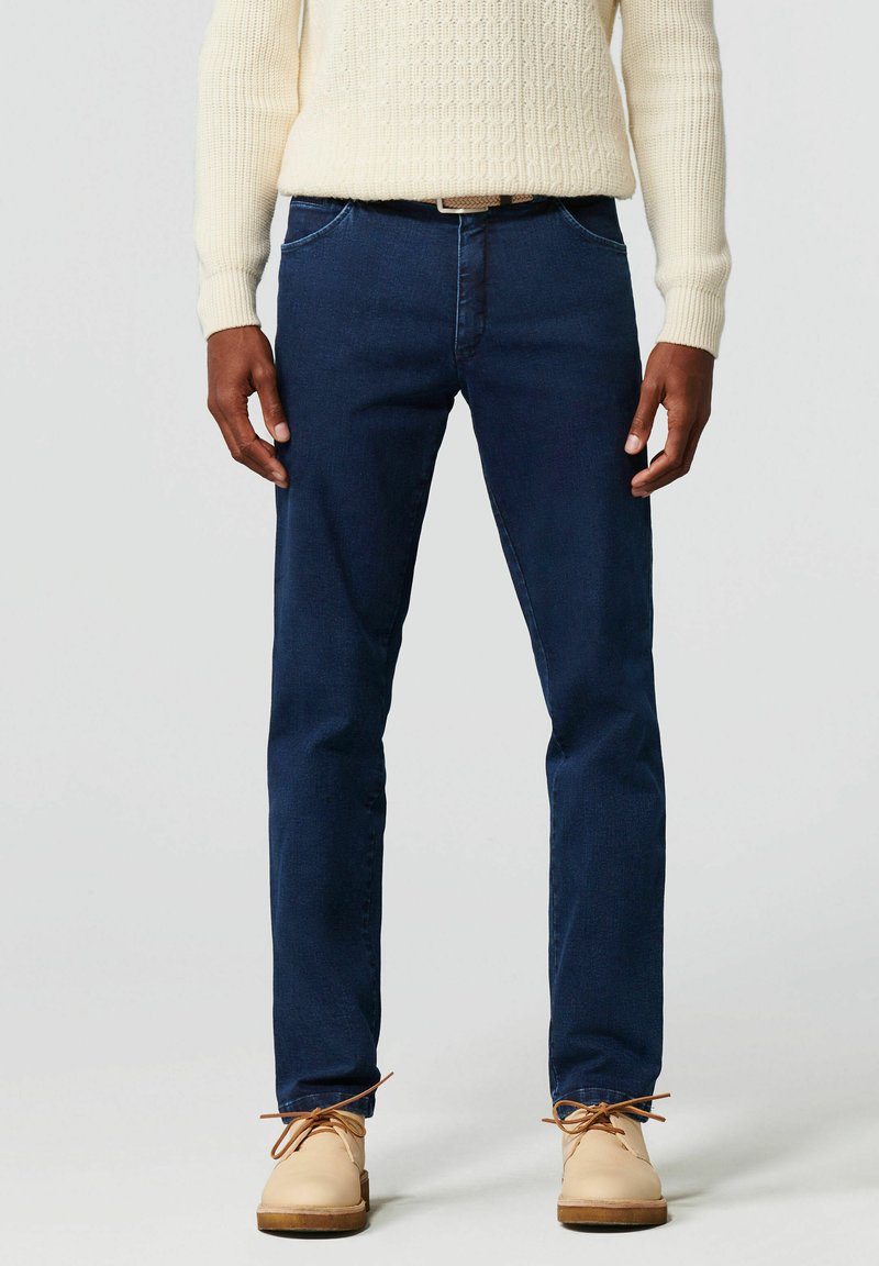 Donkerblauwe jeans met een slim fit, voorzien van voorzakken, subtiele stiksels en een zachte textuur. Draag ze met lichtbeige schoenen.