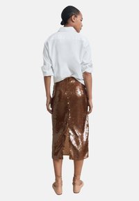 Chemise blanche à manches retroussées, associée à une jupe midi en sequins marron avec une fente dans le dos. Texture lisse et finition brillante.