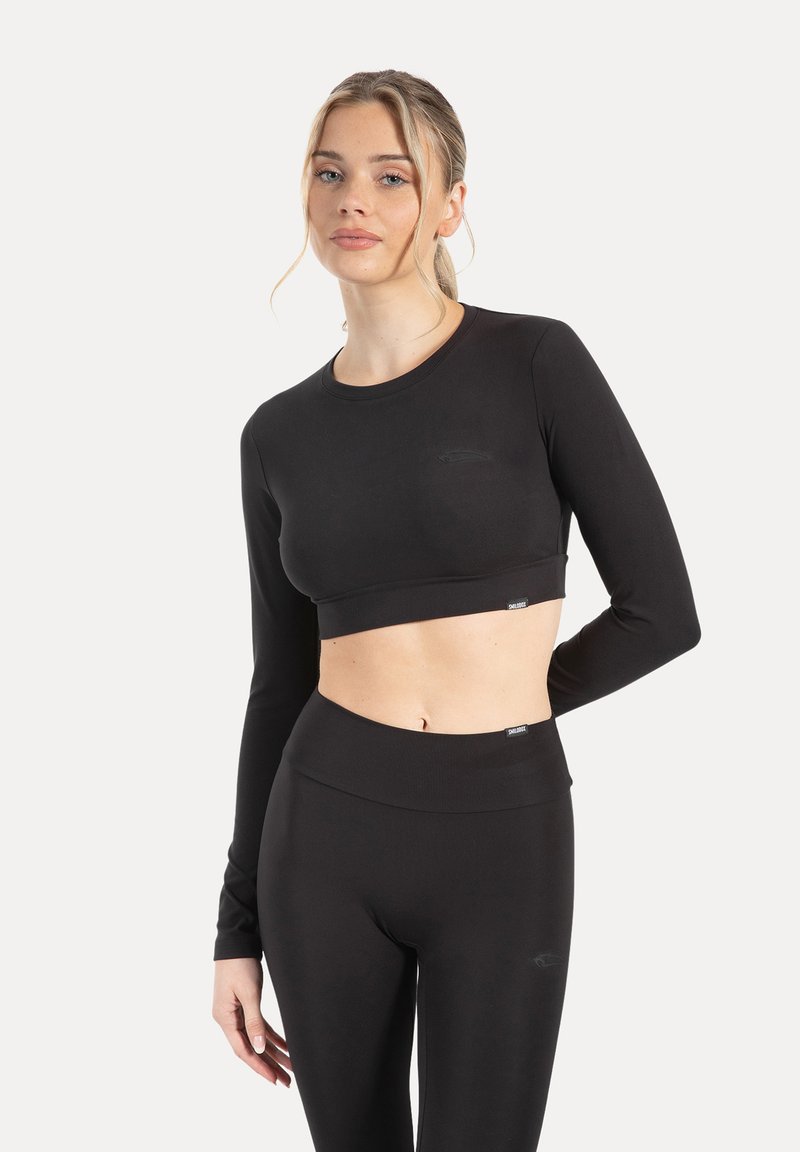 Top corto nero a maniche lunghe abbinato a leggings a vita alta, realizzati in tessuto liscio ed elastico, con un marchio discreto su entrambi i capi.