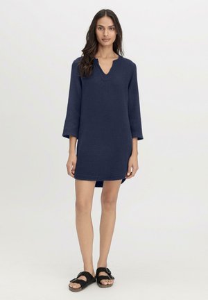 Abito blu navy, di lunghezza al ginocchio, realizzato in tessuto testurizzato con scollatura a V e maniche a tre quarti, abbinato a sandali neri.