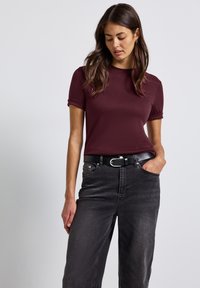 Burgundské tričko s krátkým rukávem a ohrnutými rukávy, v kombinaci s nohavicemi z černého denim s vysokým pasem a černým pásem se stříbrnou sponou.
