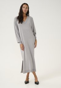 Robe longue gris en maille avec un décolleté en V subtil, ornée de manches ballons et d'une fente sur le côté, associée à des escarpins noirs à bout pointu.