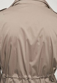 Trench-coat beige avec une texture lisse, taille cintrée, pattes d'épaule et col plié, conçu pour une coupe décontractée à l'arrière.