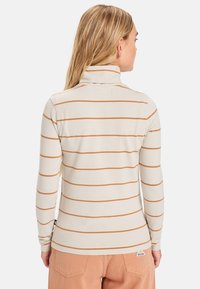 Chemise à manches longues et col haut en beige clair avec des rayures horizontales rouille, présentant une texture douce et une coupe ajustée.