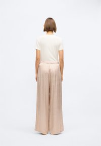 Ανοιχτό μπεζ μπλούζα συνδυασμένη με φαρδιά, μεταξένια παντελόνια με σχέδιο σε απαλό ροζ. Χαλαρή εφαρμογή με ελαστική μέση, ομαλή υφή σε όλη την επιφάνεια.