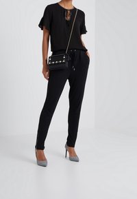 Sort kortærmet top med bånd ved halsen, parret med sorte tapered bukser og grå mønstrede højhælede sko. Sort taske med dekorative nitter.