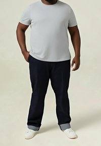 Camiseta gris de manga corta con cuello redondo, combinada con pantalones azul marino oscuro que tienen puños grises y zapatos blancos sin cordones.