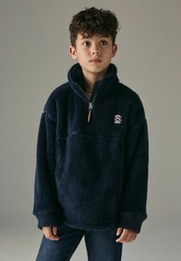 Pullover in pile di color blu navy con mezza zip, colletto alto, polsini a coste e logo ricamato sul petto. Tessuto morbido e texturizzato.