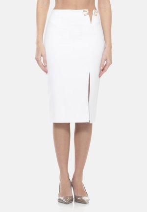 Jupe crayon blanche avec fente avant et accents décoratifs dorés à la taille, portée avec des escarpins beiges à bout pointu.