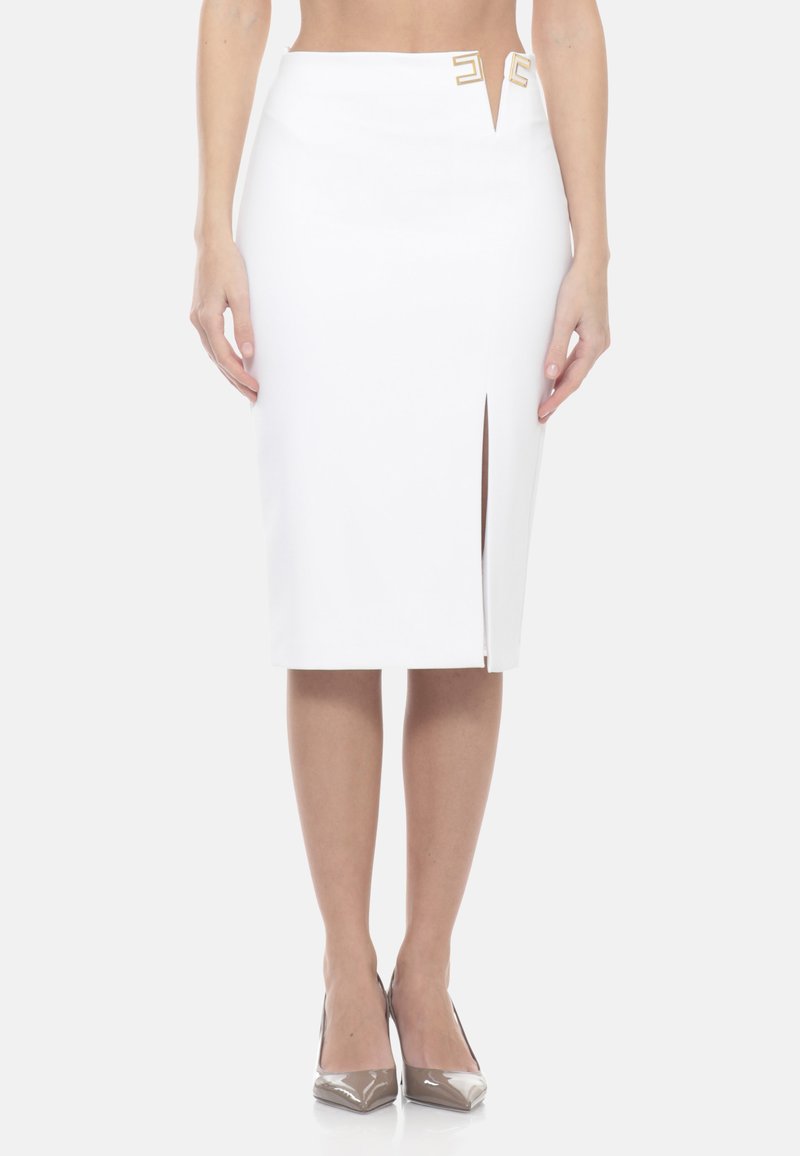 Jupe crayon blanche avec fente avant et accents décoratifs dorés à la taille, portée avec des escarpins beiges à bout pointu.