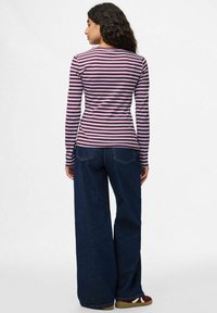 Camiseta de manga larga, de canalé, en rayas burdeos y blancas, combinada con jeans de mezclilla oscuros de pierna ancha y zapatillas multicolores.