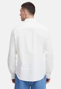 Weißes Langarmhemd mit Kragen, Rückenpasse und abgerundetem Saum. Hergestellt aus leichtem, strukturiertem Stoff, mit geknöpften Manschetten.