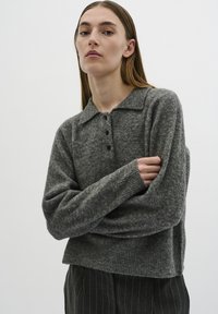 Gray knit sweater with a collared neckline, three front buttons, ribbed cuffs, and a relaxed fit. Worn with pinstriped trousers.