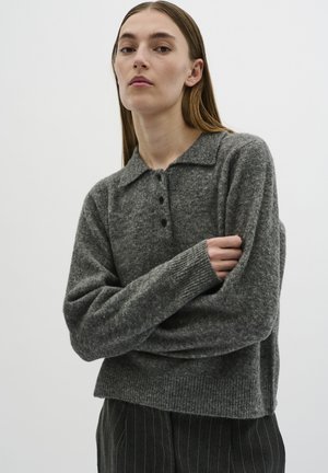 Gray knit sweater with a collared neckline, three front buttons, ribbed cuffs, and a relaxed fit. Worn with pinstriped trousers.