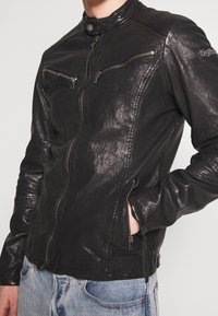 Giubbotto da moto in pelle nera con un design aderente, tasche con zip, dettagli a coste sulle spalle e collo a scatto. Finitura testurizzata.