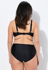 Conjunto de bikini negro que presenta un diseño de espalda deportiva y braguitas de cintura alta. La tela tiene una textura suave y un detalle mínimo.
