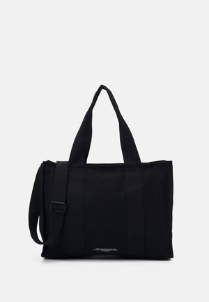 Bolsa de lona rectangular negra con asas dobles para llevar y una correa de hombro ajustable sobre un fondo claro y liso.