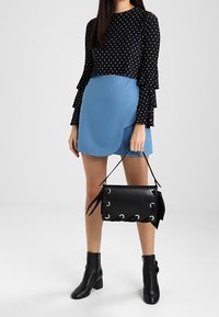 Černý top s puntíky a rozšířenými rukávy, světle modrá zavinovací sukně, černé kotníkové boty a černá kožená kabelka se stříbrnými očky.