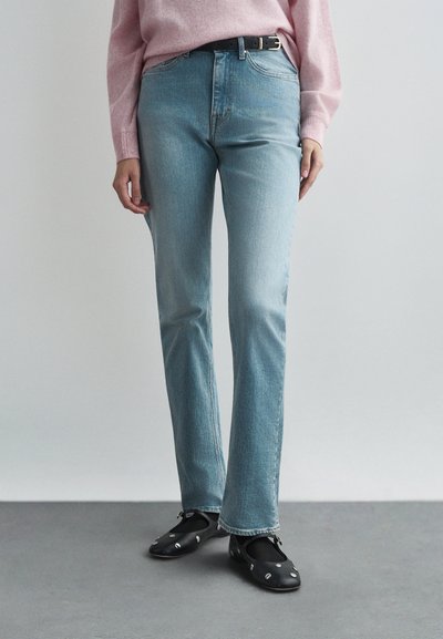 Jeans de pierna recta en azul claro, fabricados en denim, con una cintura de altura media y un ligero desvanecimiento. Combinados con zapatos negros decorados con adornos.