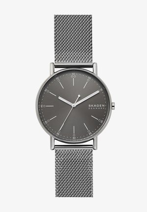 Orologio Skagen con quadrante grigio, cinturino in maglia argentata, design minimalista, indicatori delle ore e lancette eleganti. Presenta una cassa rotonda in acciaio inox.
