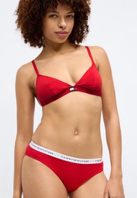 Punane puuvillane bralee õhukeste rihmade ja logo elemendiga; sobivad punased bikiinid valge vöökohtadega, mille peal on silt "TOMMY HILFIGER." Sujuv tekstuur.