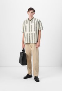 Short-sleeve shirt with a green and cream stripe pattern, black bag, beige trousers, black shoes; relaxed fit and textured fabric.
