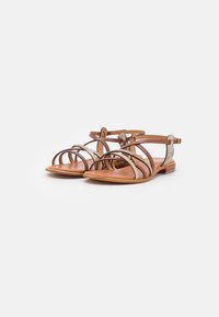 Sandalias de cuero marrón con múltiples correas cruzadas, que presentan un sutil acento metálico y una suela plana. Diseño abierto en la parte delantera para mayor transpirabilidad.