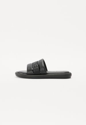 Sandalia deportiva negra con suela gruesa acolchada y tira ancha con texto en relieve sutil, mostrada de perfil sobre fondo blanco liso.