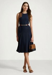 Tumesri kleit pruunide õlavarre aktsentidega, vooderdatud talje ja laienev seelik. Pruun vööp ja pruun-must käekott. Hallid avatud varvastega sandaalid.