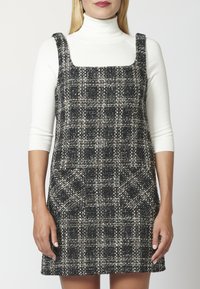 Abito a quadri in bianco e nero con scollatura quadrata, tessuto texturizzato e due tasche anteriori. Senza maniche e con spalline larghe.