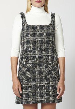 Robe à carreaux noir et blanc avec un décolleté carré, tissu texturé et deux poches avant. Sans manches avec des bretelles larges.