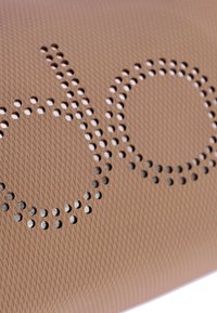 Un material texturizado en beige claro presenta un diseño perforado con cortes circulares que deletrean "dob". La superficie es suave con un patrón de malla fina.