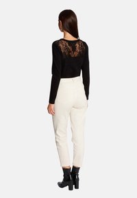 Haut noir à manches longues avec un dos en dentelle. Associé à un pantalon couleur crème et à des bottines noires. Textures lisses et ajustées.