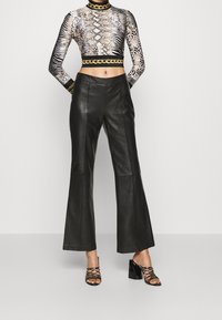 Cropped long-sleeve top with animal print motifs in gold and black; high-waisted black leather flared pants; heeled black lace-up sandals.